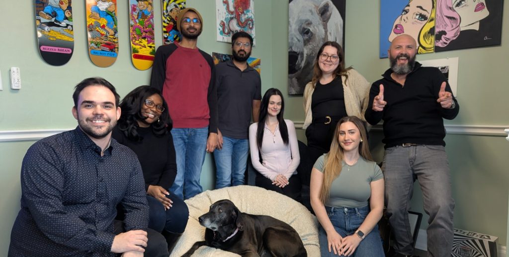 A team photo of the Spinealytics team. From left to right: Mike, Chanel, Sam, Qasid, Emily, Brittany, Tara, Quinn, with Winnie on her dog bed in the center.